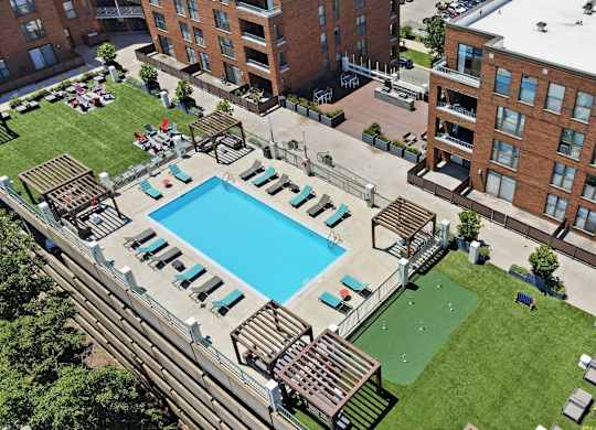 An aerial view of a building with a rooftop pool in the middle and social deck with AstroTurf, firepits, grills, and assorted seating around it.