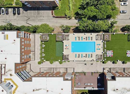 An aerial view of a building with a rooftop pool in the middle and social deck with AstroTurf, firepits, grills, and assorted seating around it.