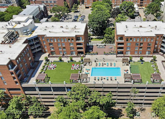 An aerial view of a building with a rooftop pool in the middle and social deck with AstroTurf, firepits, grills, and assorted seating around it.