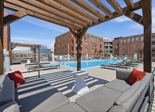 A wooden pergola over a rooftop pool area with lounge chairs and cushions.
