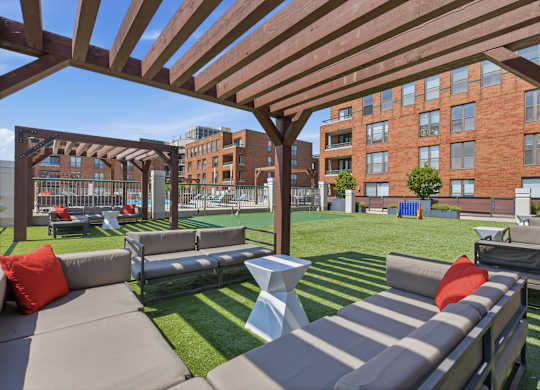 A rooftop patio with a white table and chairs under a wooden pergola with putting green and outdoor games in the background.