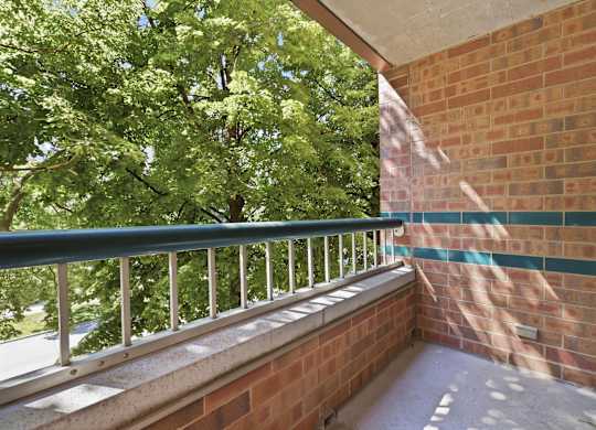 A balcony with a green railing and a brick wall.