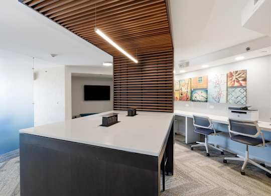 Main room of the business center with a community work table with a TV and printing in the background.