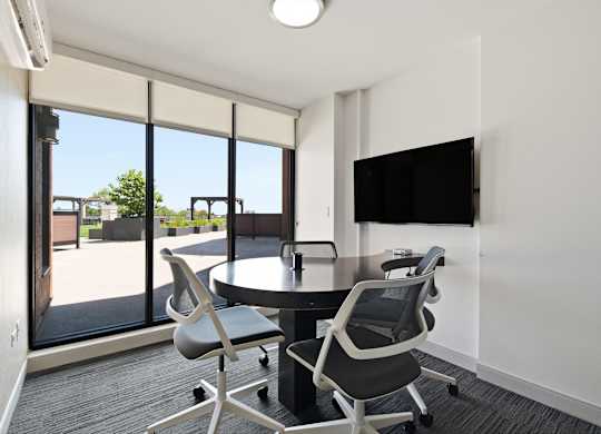 A conference room with a table, chairs, and a television on the wall.