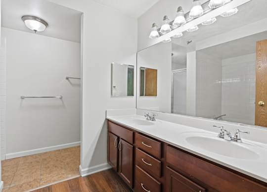 A bathroom with double vanity, full wall mirror, medicine cabinet, and brown cabinets.