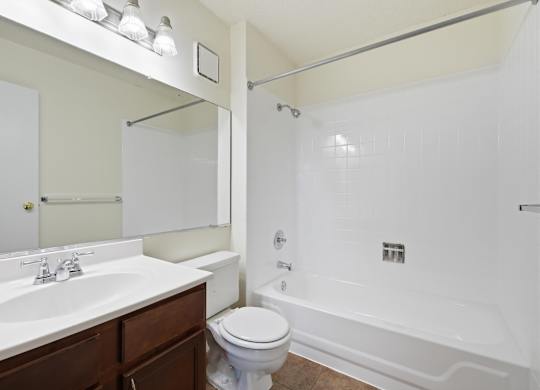 A white bathroom with a toilet, sink, mirror, and tiled bathtub.