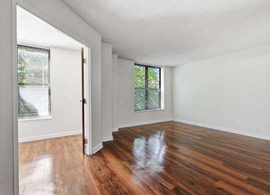 A bedroom with wooden floors, window, and attached den.
