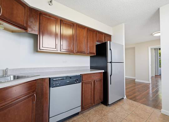A kitchen with brown cabinets and a stainless steel appliances: dishwasher and fridge.