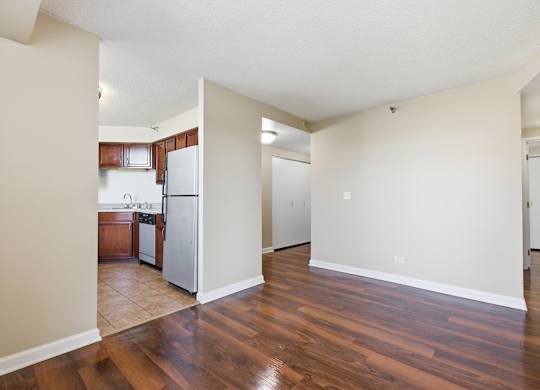 A living room with kitchen in the background that has brown cabinets and stainless steel appliances.