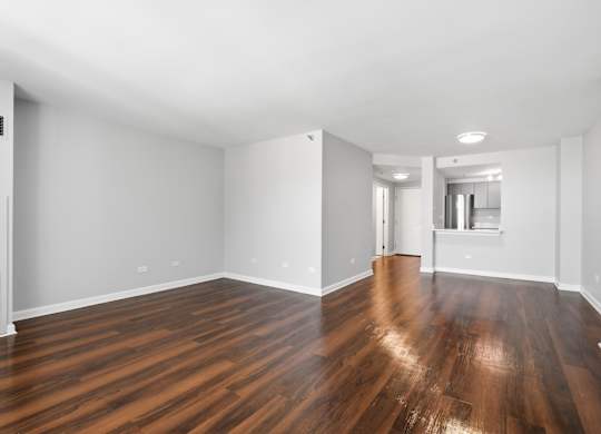 A renovated studio living and bedroom space with wooden floors and kitchen pass through in the background.