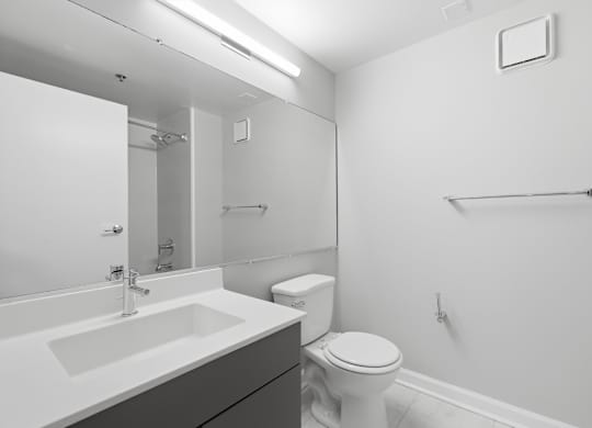 A modern renovated bathroom with full wall mirror, sink, and toliet.