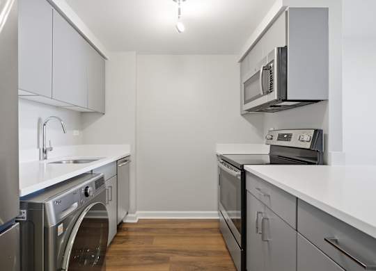 A renovated kitchen with a stainless steel refrigerator, microwave, oven, and 2-in-1 washer/dryer.