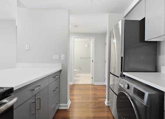 A renovated kitchen with a stainless steel refrigerator, microwave, oven, and 2-in-1 washer/dryer and bathroom in the background.