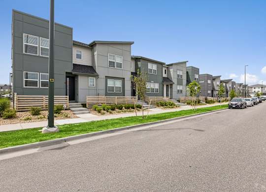 A street view of a residential area with houses on the side and cars parked on the side of the road.