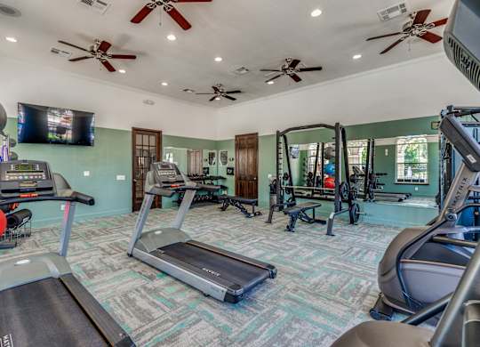 A gym with treadmills, elliptical machines, and a television.