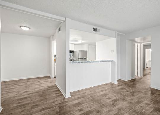 an empty living room with a kitchen in the background