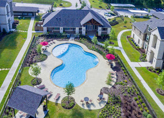 An aerial view of a swimming pool surrounded by a landscaped garden and residential buildings.