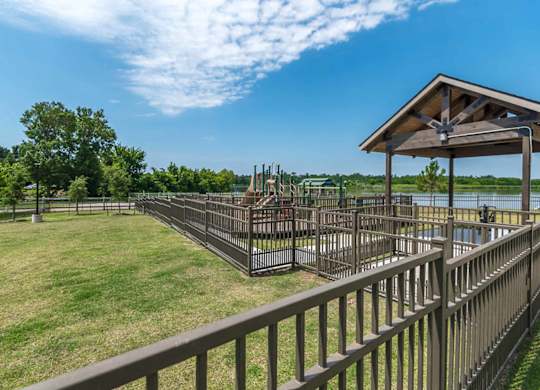 A playground with a wooden roof and metal bars is surrounded by a fence.