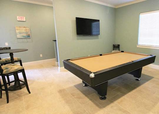 A room with a pool table and a television mounted on the wall.