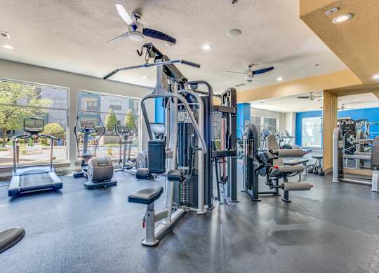 A spacious gym with a variety of equipment including treadmills, weight machines, and a ceiling fan.