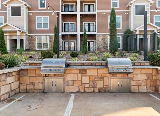 A wall of apartment buildings with a stone wall and grills in front.