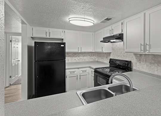 A black refrigerator is in a kitchen with white cabinets.