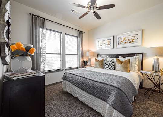 A bedroom with a large bed, a ceiling fan, and a side table with a lamp.