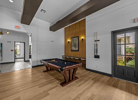 A pool table is in the middle of a room with a door to the left and a window to the right.