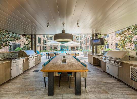 A long wooden table is in the middle of a patio with barbecue grills on either side.