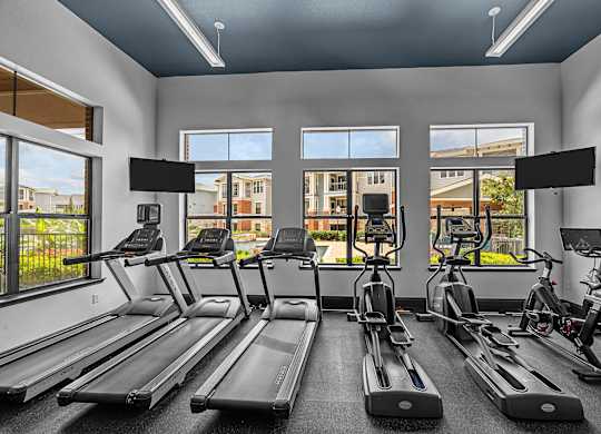 A gym with treadmills, exercise bikes, and a view of the outside.