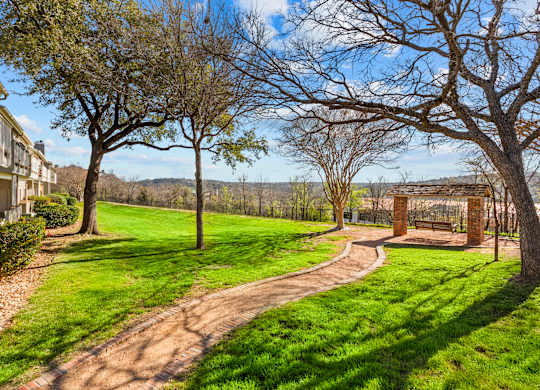 A pathway leads through a grassy area with trees and a bench.