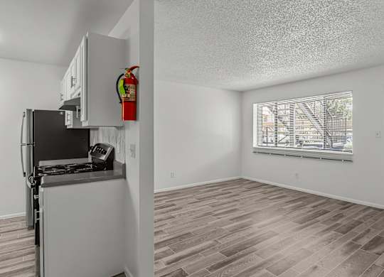 the living room and kitchen of an apartment with a refrigerator and a window