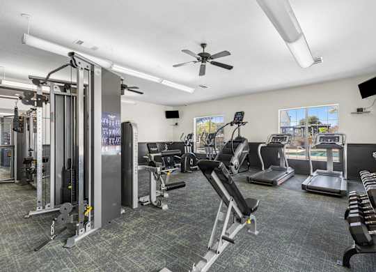 A well-equipped gym with various exercise machines and a ceiling fan.