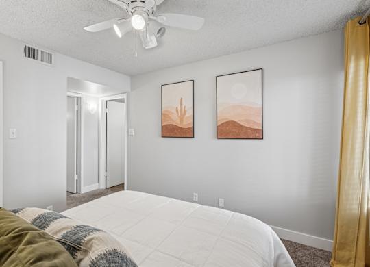 A bedroom with a bed, a ceiling fan, and two framed pictures on the wall.