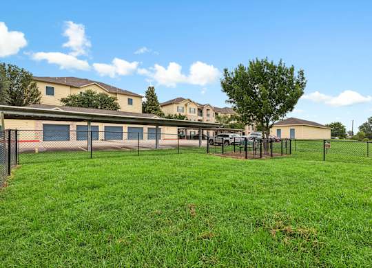 A grassy field with a fence and a tree in front of a building.