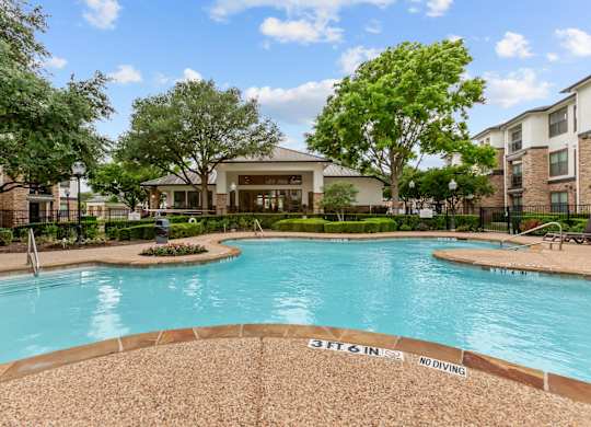 A pool surrounded by trees and a building in the background.