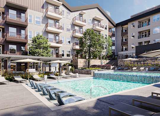 A large swimming pool surrounded by lounge chairs and umbrellas in front of apartment buildings.