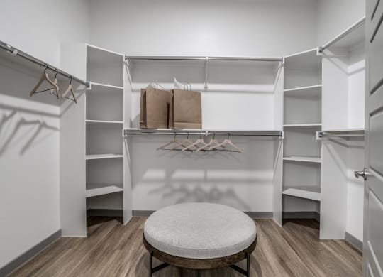 a walk in closet with a round stool in the middle