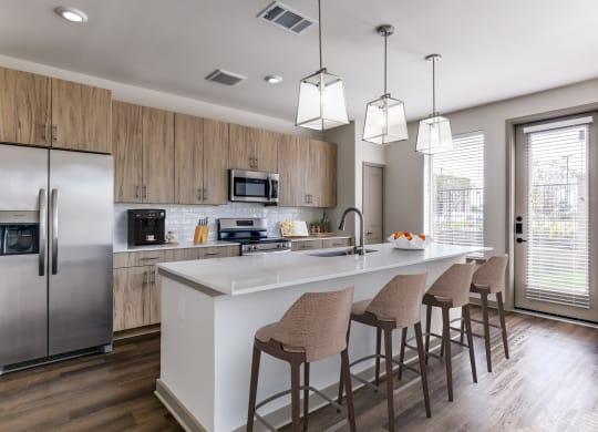 a kitchen with a large island with bar stools and a stainless steel refrigerator