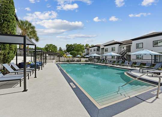 A swimming pool surrounded by sun loungers and umbrellas.