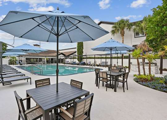 A table with chairs and umbrellas is set up near a pool.