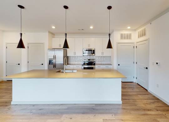 A kitchen with a white island and pendant lights.
