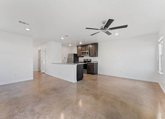 an empty living room with a kitchen and a ceiling fan