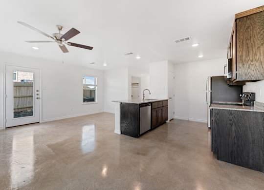 an empty living room with a kitchen and a ceiling fan