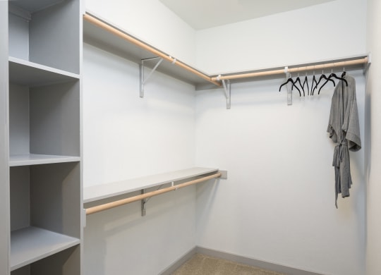 a walk in closet with a white wall and shelves and a rack with a robe