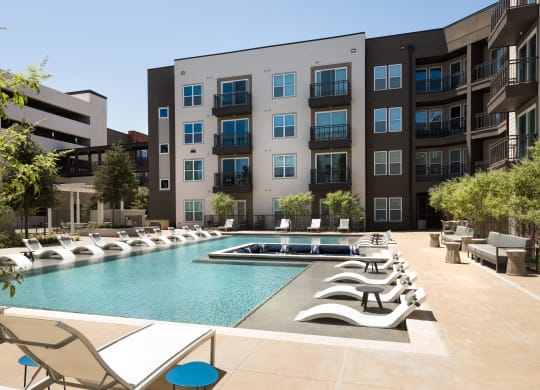 a pool with lounge chairs in front of an apartment building