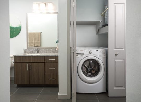 a white washer and dryer in a bathroom with a sink and a mirror