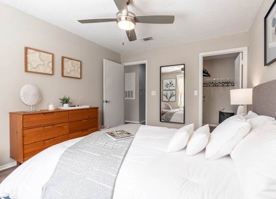 A bedroom with a large bed, a ceiling fan, and a dresser.