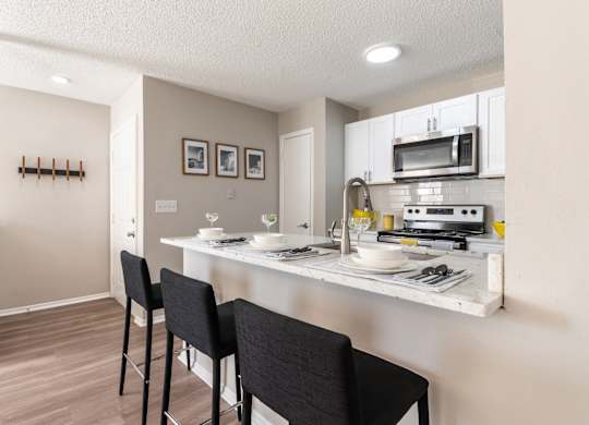 A kitchen with a white counter and black chairs.