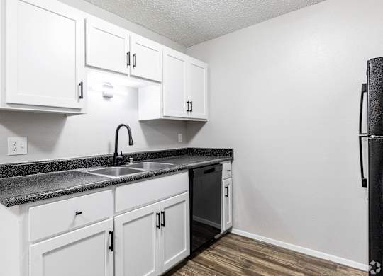 A kitchen with white cabinets and a black fridge.